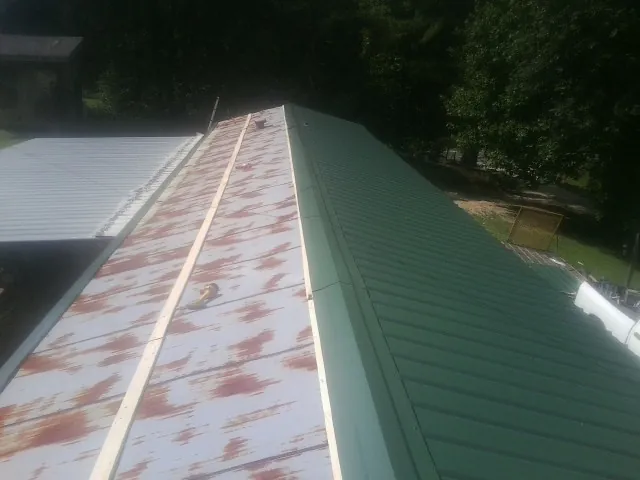 Old rusted panels beside newly installed green metal roofing — Wind Damage Roof Repair by Roofing Brothers in Yoder