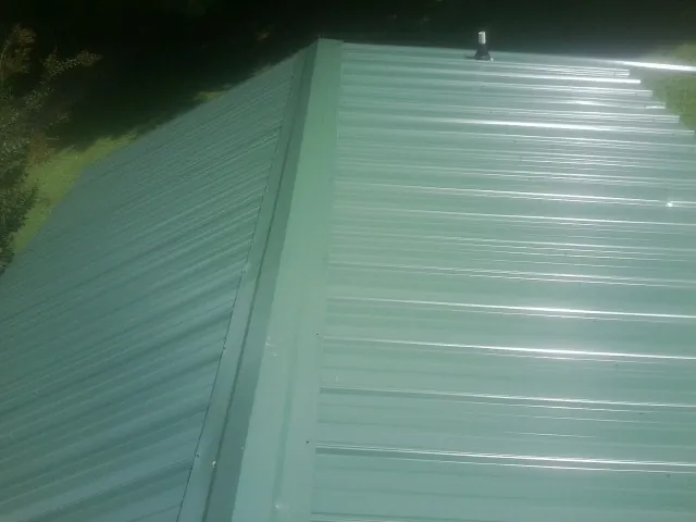 New green metal panels meeting at the ridge of a roof — Flat Roof Repair work by our crew in Yoder