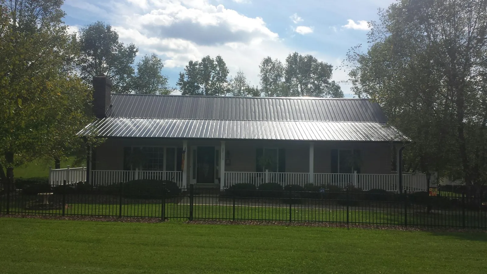Gray metal roof on a brick ranch with a full width front porch — Gutter Guard Installation work by our crew in Yoder