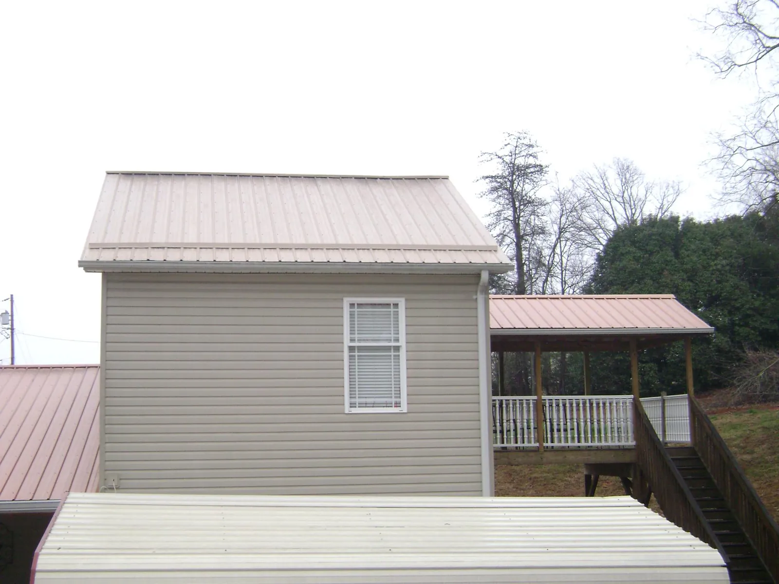 Tan metal roofs on a two story addition and attached porch, from a Roof Replacement job in Yoder
